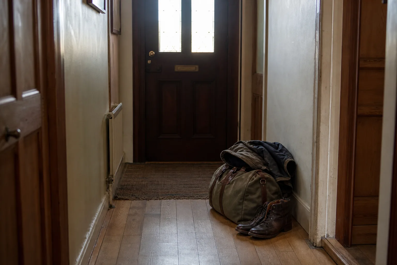 A canvas holdall and a winter coat set down on the floor inside a front door